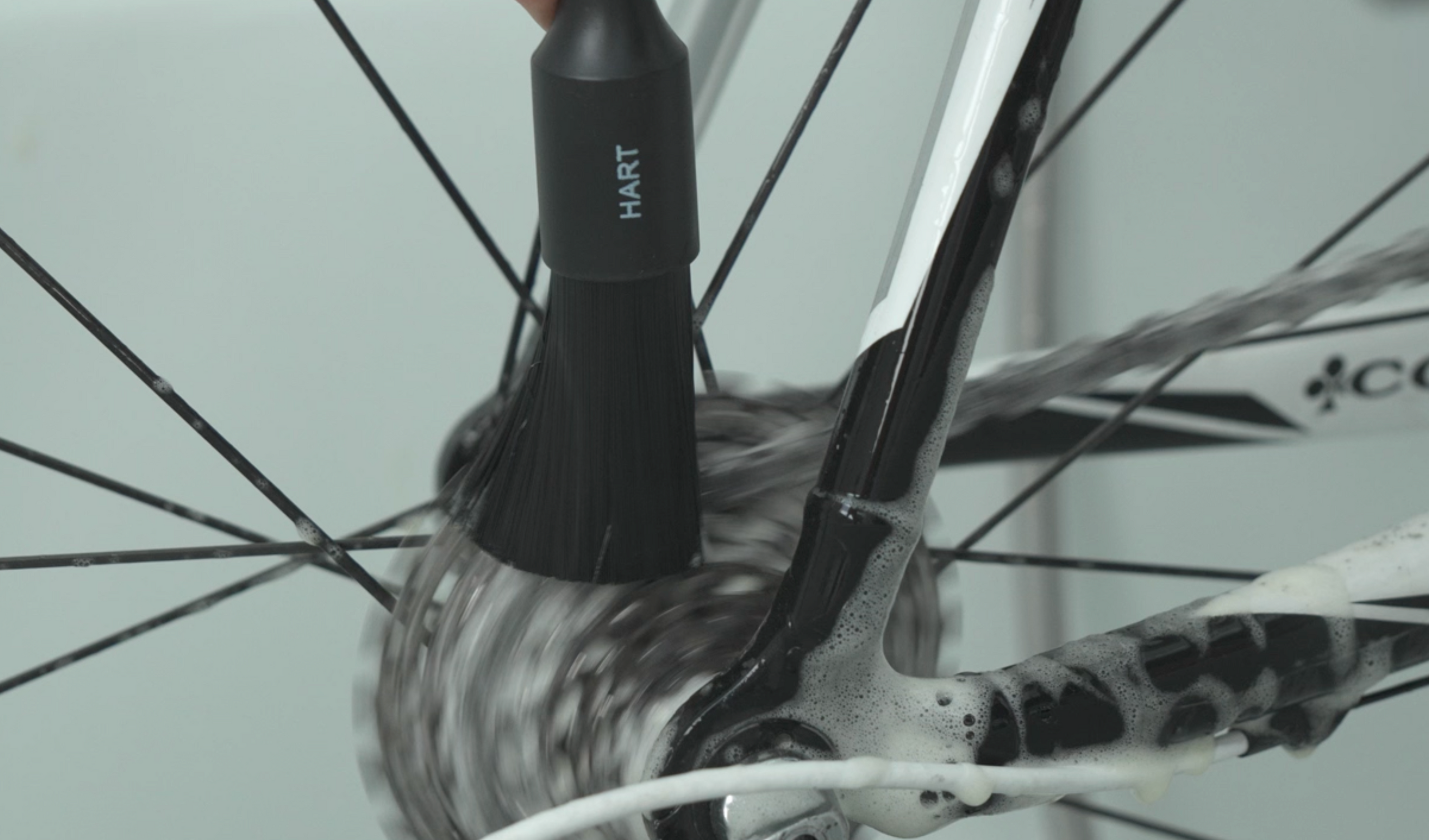 Eine Nahaufnahme von jemandem, der das Pinselset - Fahrrad Detailing verwendet, um die hintere Kassette und die Schaltung eines Fahrrads zu reinigen, wobei Seife und Wasser auf den Komponenten und dem Rahmen sichtbar sind.