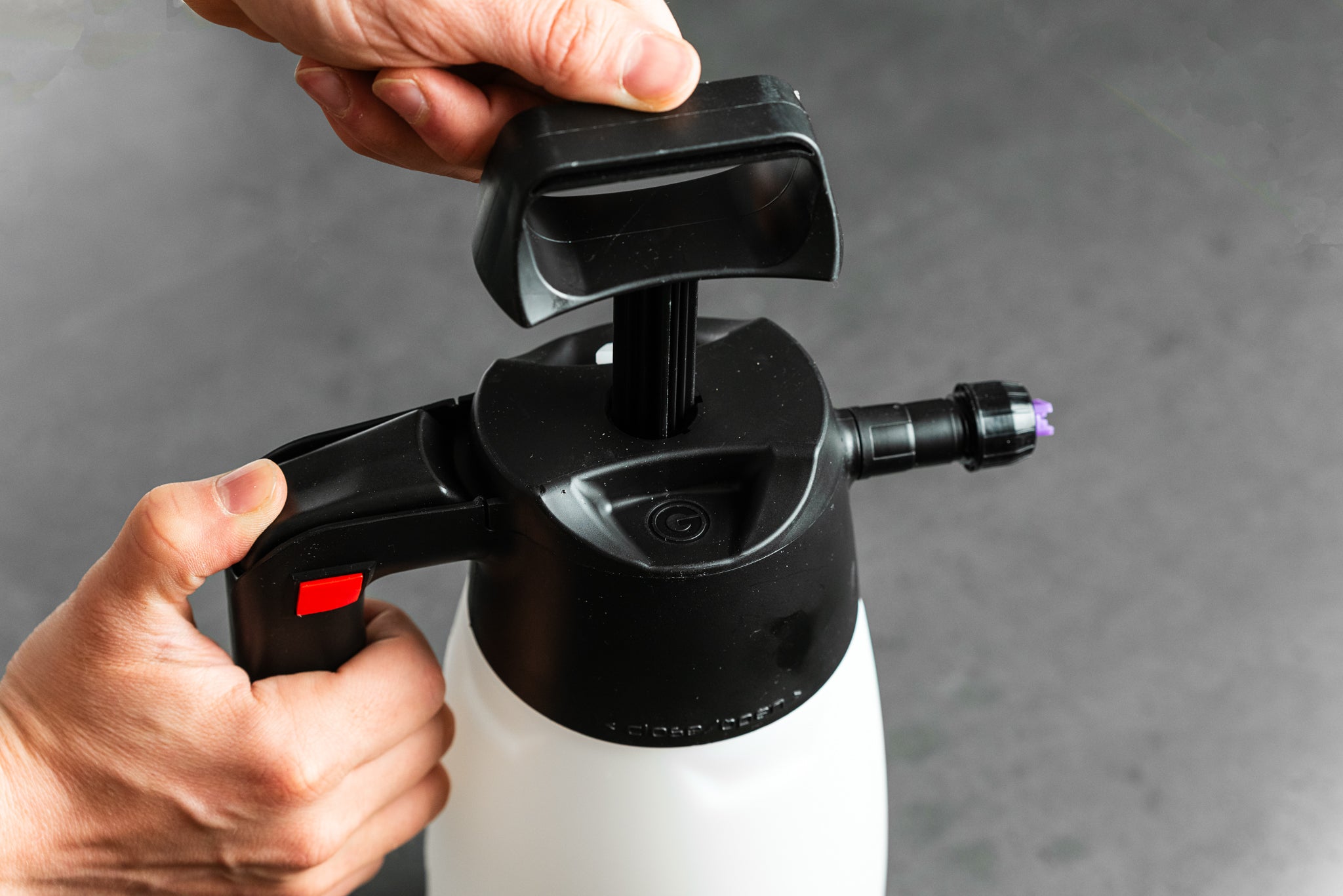 Eine Nahaufnahme der Hände, die den IK FOAM Pro 2 - Pumpsprüher benutzen, wobei der obere Griff vor einem grauen Hintergrund gedrückt wird - perfekt für die Fahrradreinigung dank des effektiven Schaumsystems.