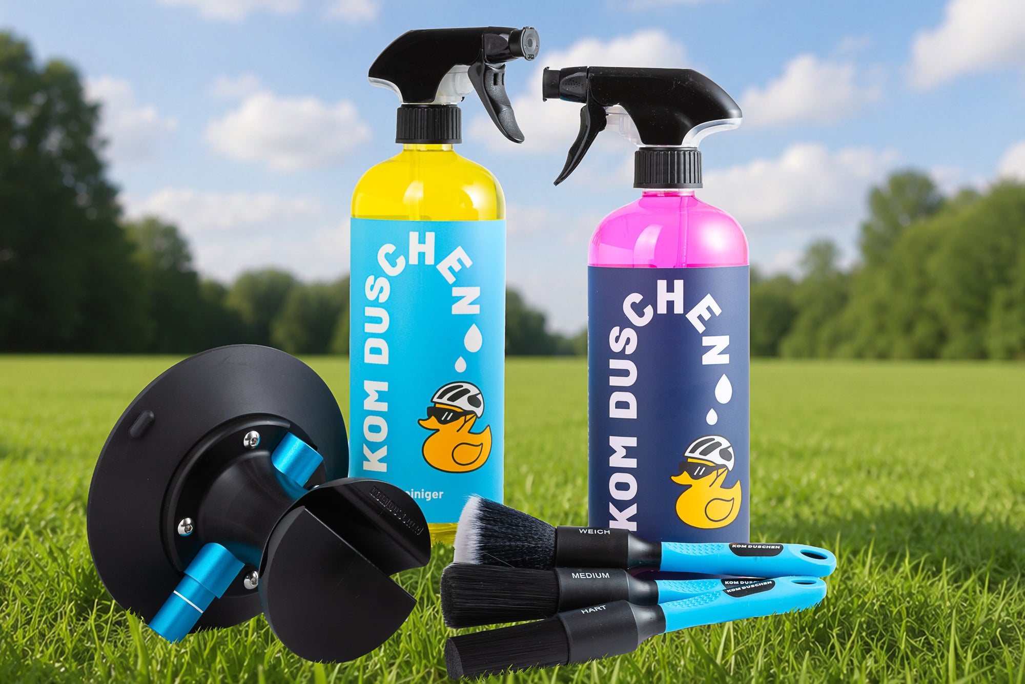 Das Profi - Set, bestehend aus zwei Sprühflaschen mit leuchtend blauen und rosafarbenen Etiketten, zwei Bürsten mit blauem Stiel und einem schwarz-blauen Reinigungswerkzeug, wird auf einer Wiese mit Bäumen und blauem Himmel im Hintergrund präsentiert.