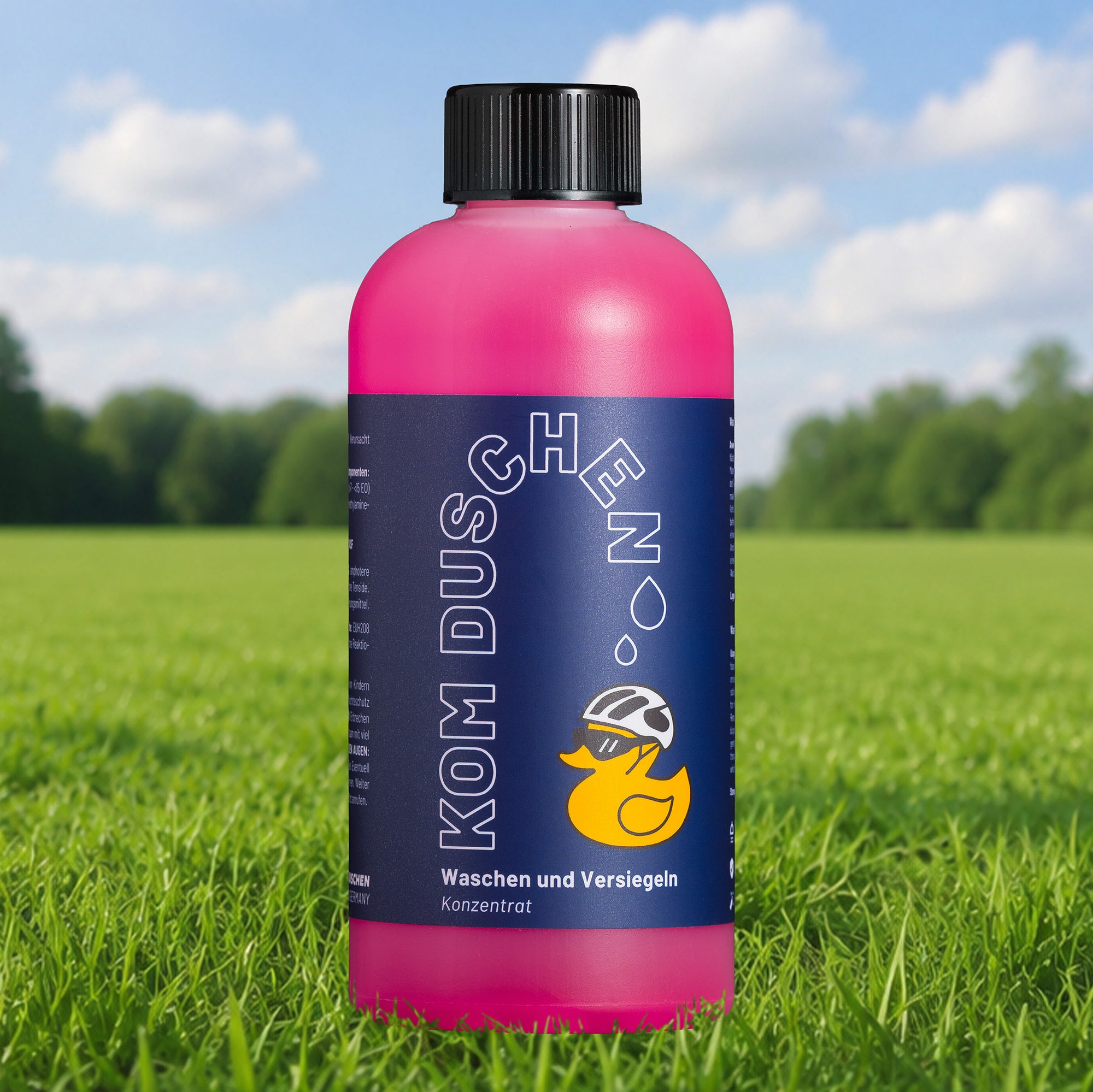 Eine Flasche „Waschen und Versiegeln – Konzentrat“, ein rosa Reinigungskonzentrat mit einer Comic-Ente auf dem Etikett, steht auf grünem Gras vor einem unscharfen Außenhintergrund. Dieser vielseitige Reiniger mit Wachsanteilen eignet sich perfekt für die schonende Fahrradreinigung und bietet zusätzlichen Lackschutz.